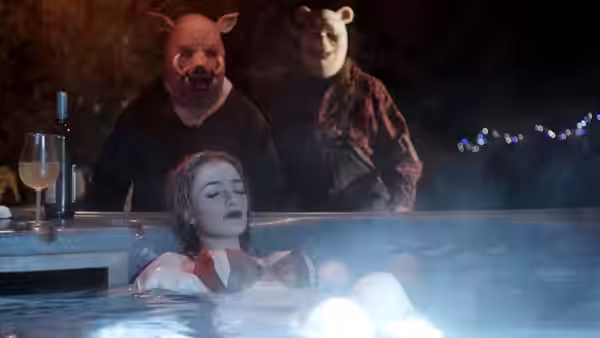A woman reclines in a steaming pool with two masked figures standing behind her