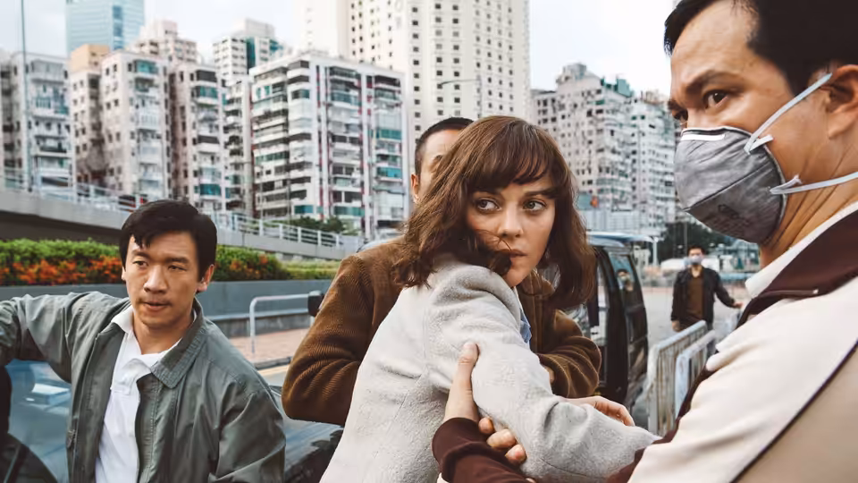 Marion Cotillard held by two men on a city street