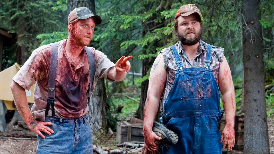 Tucker (Alan Tudyk) points while standing with Dale (Tyler Labine) in a forest