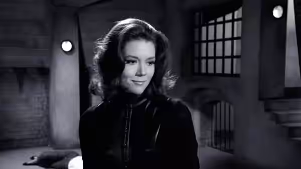 Emma Peel (Diana Rigg) smiling inside a dimly lit stone dungeon