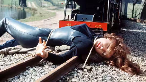 Emma Peel (Diana Rigg) tied to railroad tracks before an oncoming train