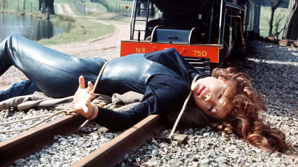 Emma Peel (Diana Rigg) tied to railroad tracks before an oncoming train