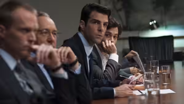 Peter Sullivan (Zachary Quinto) seated at a table with executives during a meeting