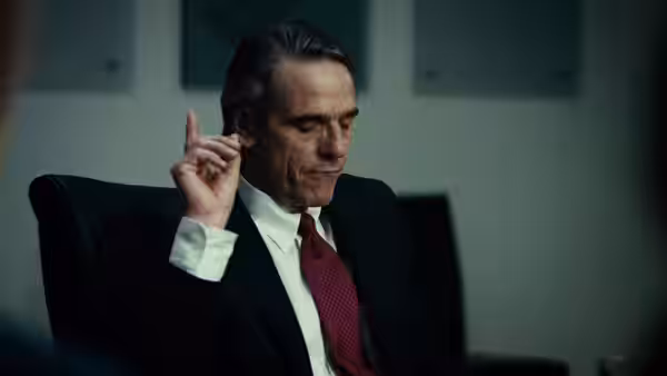 John Tuld (Jeremy Irons) seated thoughtfully with hand raised near his head