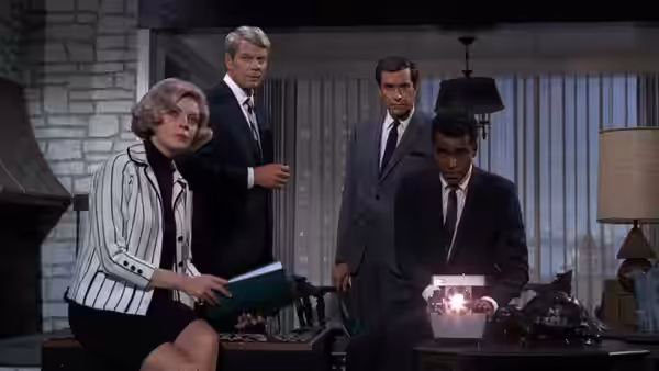 Cinnamon Carter (Barbara Bain) holds a folder while Barney Collier (Greg Morris) examines a device