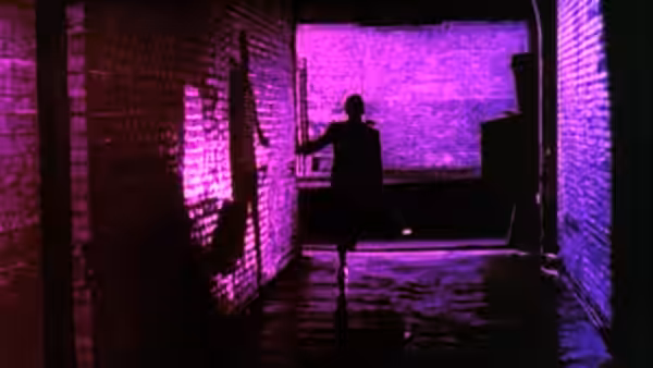 A silhouetted figure running through a purple-lit brick alleyway at night