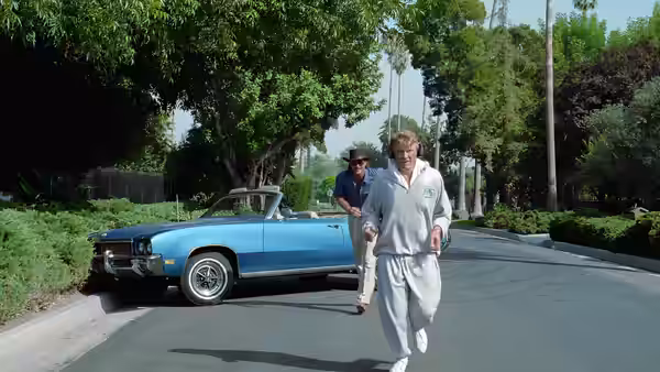 a man in a white tracksuit running on a suburban street near a blue car