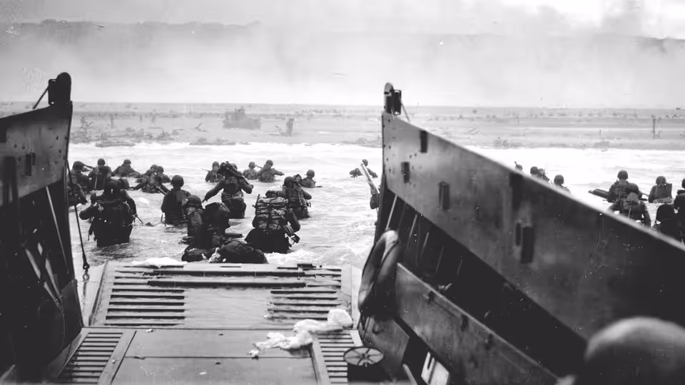 Soldiers wading from a landing craft into shallow surf toward shore