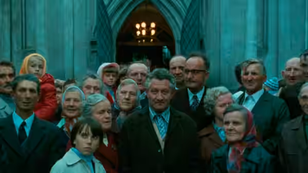 Group of men and women gather before large stone building with arched entrance