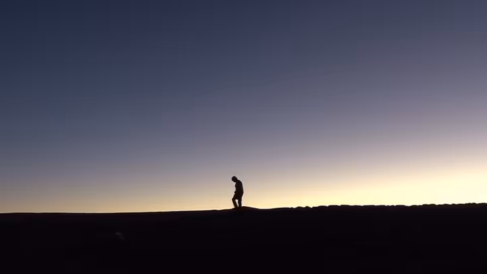 A lone figure walks along a dark desert ridge beneath the fading sky