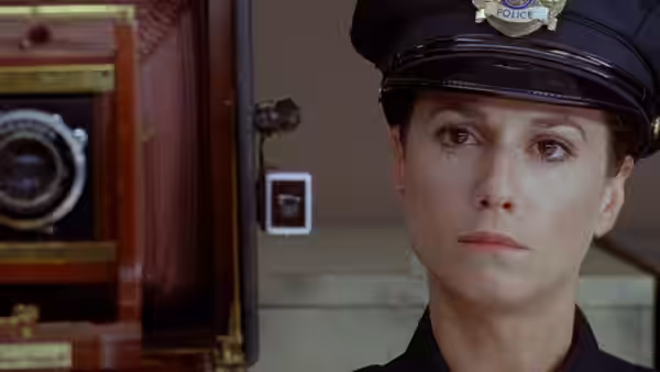 Ed (Holly Hunter) in police cap stands beside an old wooden camera