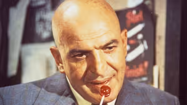 Kojak (Telly Savalas) smiles with a lollipop in his mouth