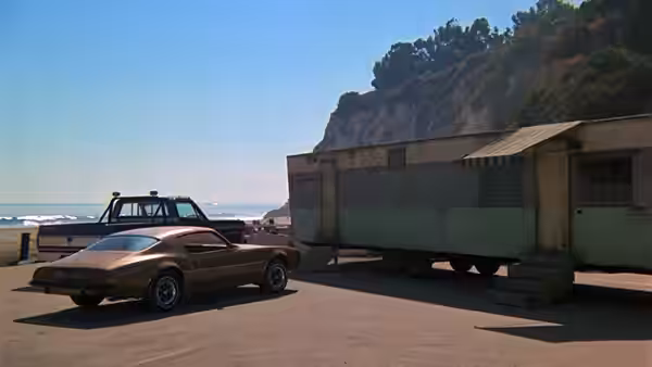 a brown car parked beside a truck near a building by the coast
