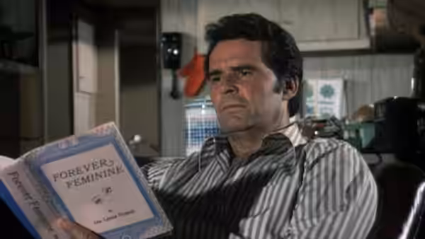 Jim Rockford (James Garner) reads a book titled Forever Feminine while seated indoors