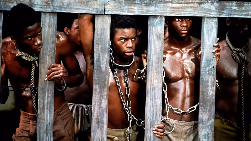Shirtless men with metal chains around their necks grip wooden bars