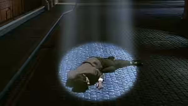 A man lies sprawled in a pool of light on a dark cobbled street
