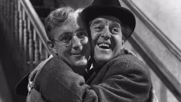 Two smiling men embrace beside a staircase
