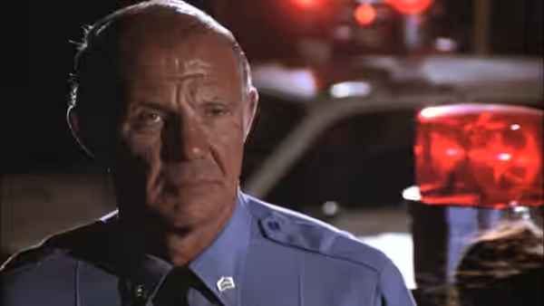 Senior police officer standing before a patrol car at night