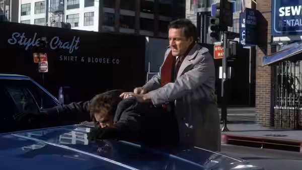 Detective pinning a man onto the hood of a blue car