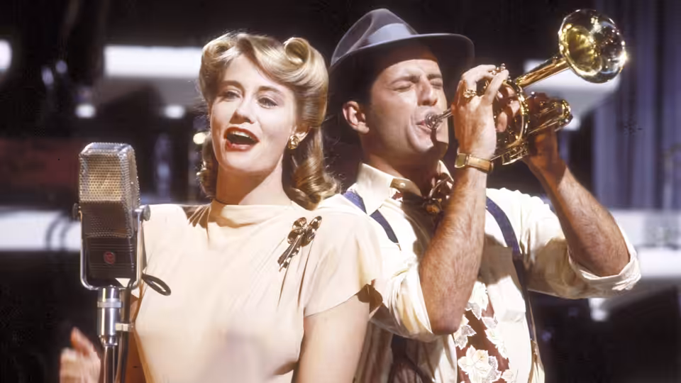 Blonde woman singing into vintage microphone as man plays trumpet
