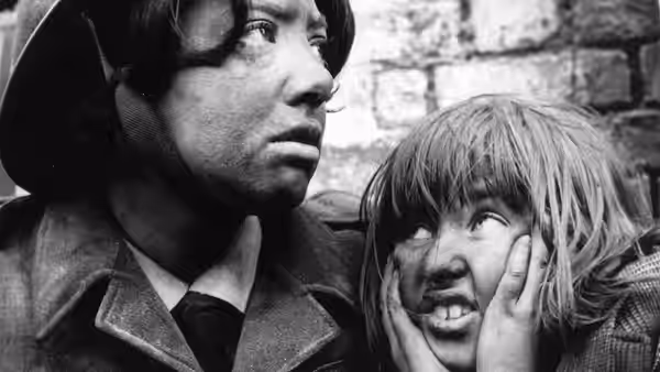 A helmeted man stands beside a child holding their cheeks and looking up