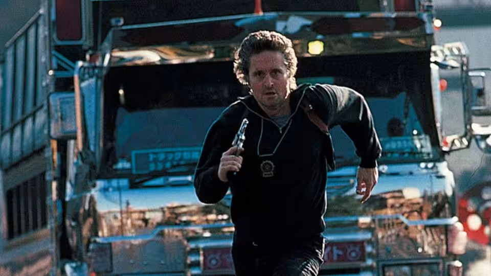 Nick Conklin (Michael Douglas) runs with a gun in front of parked trucks