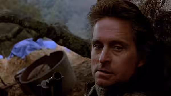 Nick Conklin (Michael Douglas) crouches beside a rifle in the rocky countryside