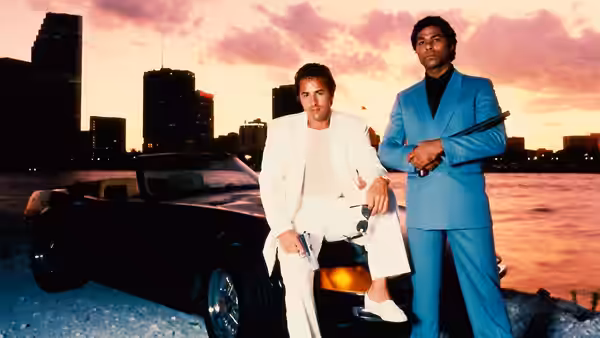Sonny Crockett (Don Johnson) and Rico Tubbs (Philip Michael Thomas) with guns beside a black car at dusk