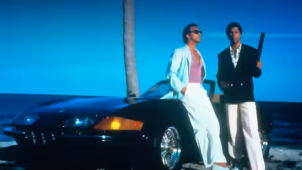 Sonny Crockett (Don Johnson) and Rico Tubbs (Philip Michael Thomas) with guns beside a black car by the ocean