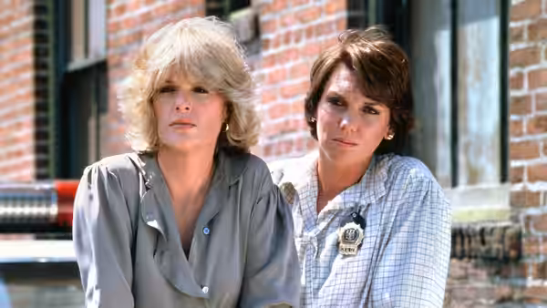 Christine Cagney (Sharon Gless) and Mary Beth Lacey (Tyne Daly) seated by a brick wall