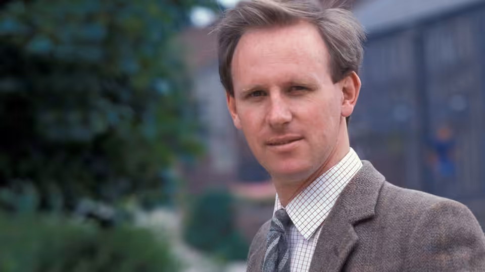 Dr Stephen Daker (Peter Davison) standing outdoors in a tweed jacket and tie