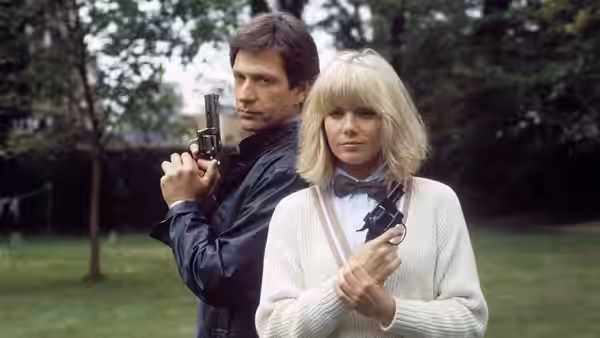 Dempsey (Michael Brandon) and Makepeace (Glynis Barber) holding guns in a garden