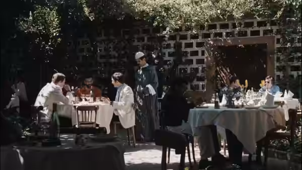 Diners sit at outdoor restaurant tables as a waiter stands among them