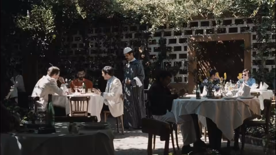 Diners sit at outdoor restaurant tables as a waiter stands among them