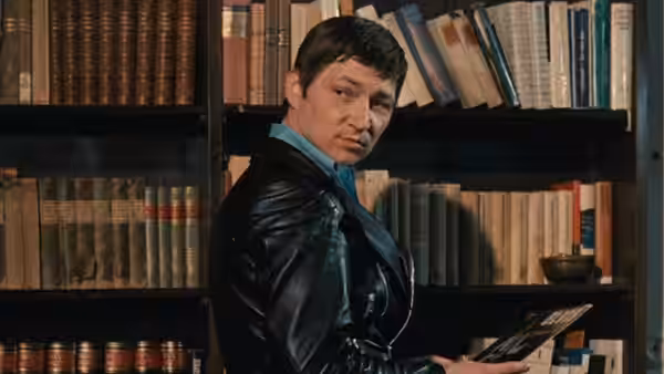 A short-haired man in a leather jacket browses bookshelves