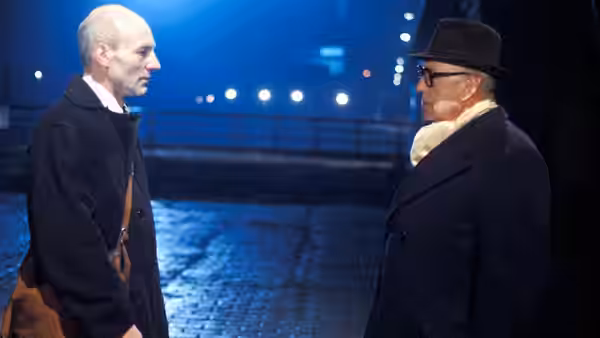 George Smiley (Alec Guinness) facing a man on a nighttime cobblestone street