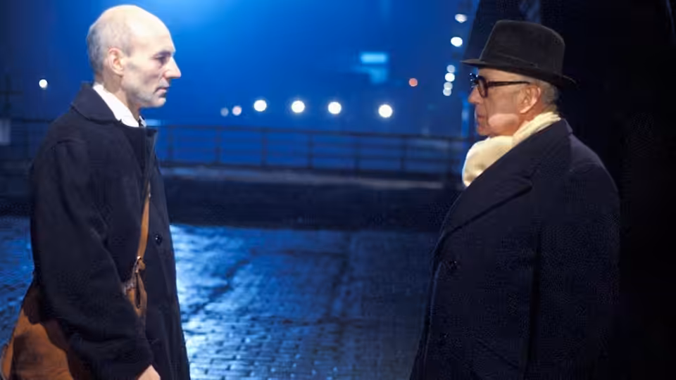 George Smiley (Alec Guinness) facing a man on a nighttime cobblestone street