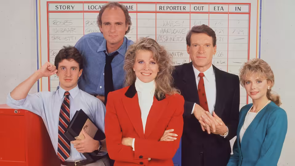 Murphy Brown (Candice Bergen) stands with her news team before a whiteboard