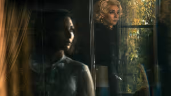 Woman with short hair seen through window beside blonde figure outside