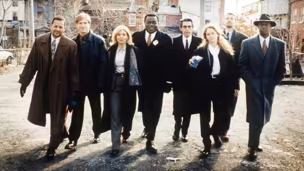 A group of men and women in suits walk across an open lot