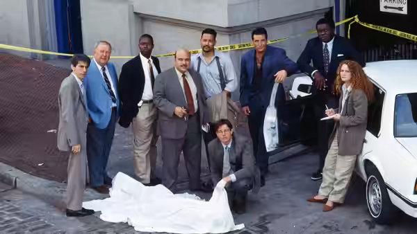 Detectives gather around a covered body on the street by a car
