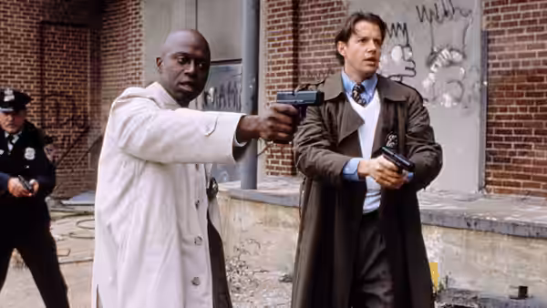 Two armed men stand ready with guns drawn near a brick building