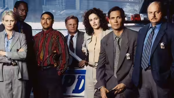 Team of detectives posing together in front of a police precinct vehicle