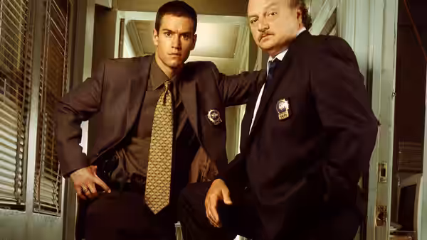 John Clark Jr. (Mark-Paul Gosselaar) and Andy Sipowicz (Dennis Franz) posing in a hallway