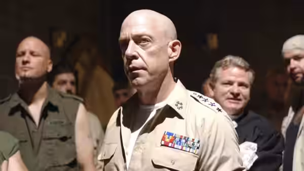 Bald man in uniform stands among inmates in a prison common area
