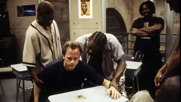 Men gather around a table with a bloodstain in a prison interview room