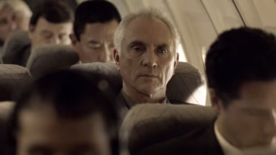 Wilson (Terence Stamp) seated among passengers on an airplane