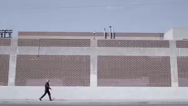 Wilson (Terence Stamp) walking past a long brick wall