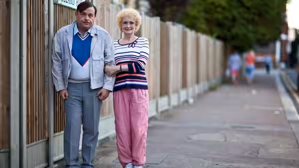 A man and woman stand close together on a quiet suburban pavement