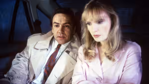 Robert Lindsay as Michael Murray seated beside a blonde woman in pink